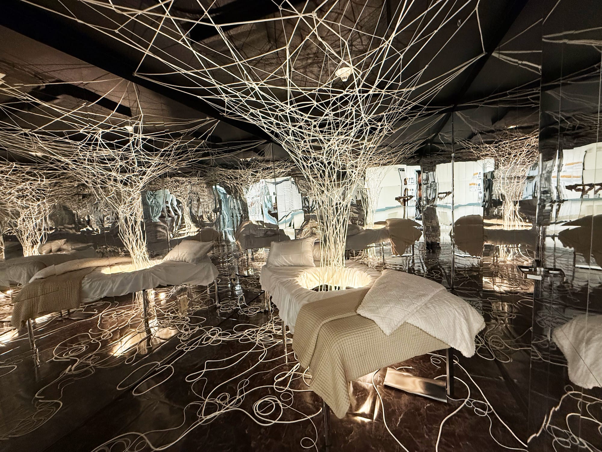 a hospital room installation transformed by embedded lights and string structures emerging from beds and across floors
