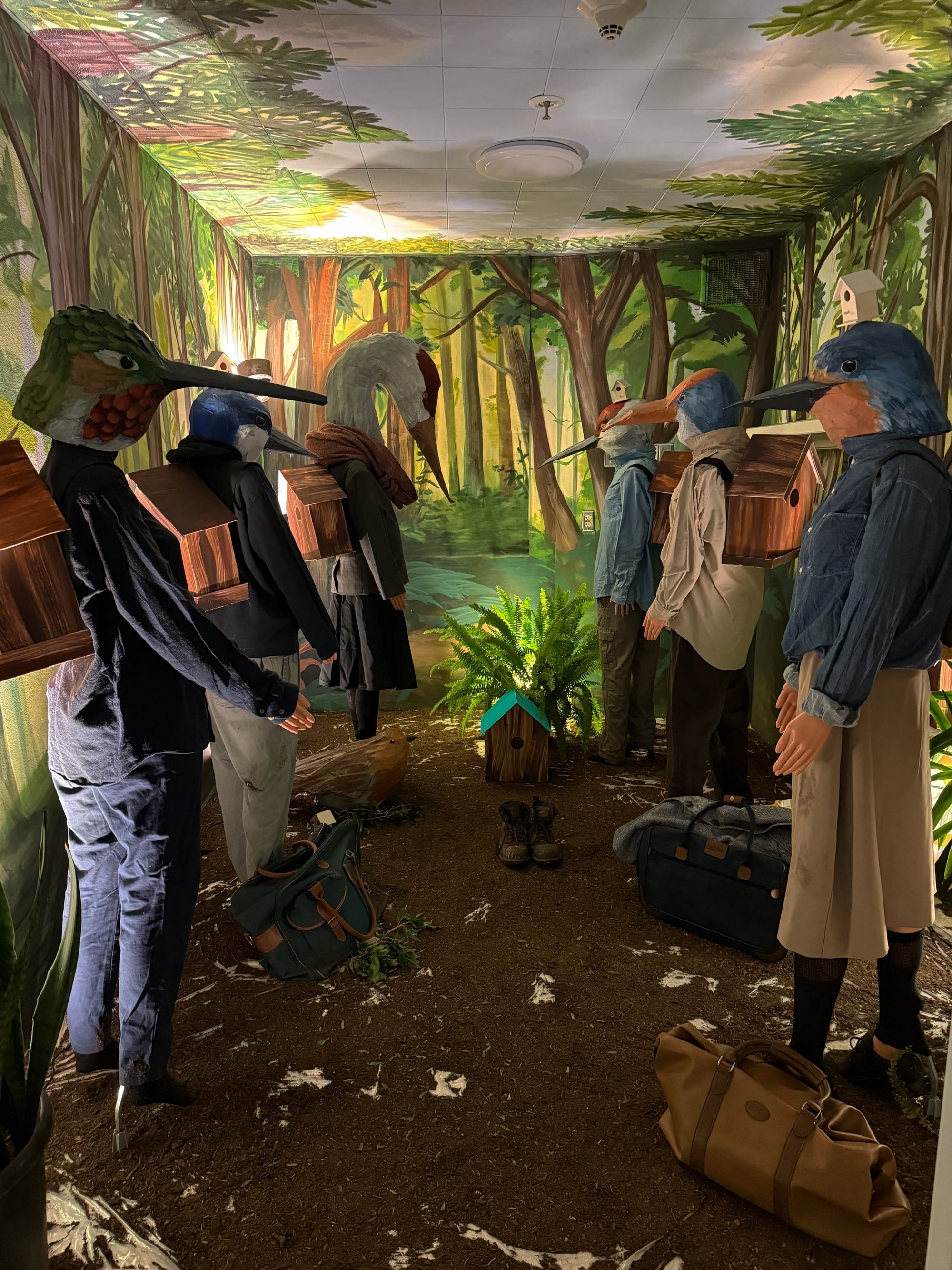 a hospital room installation transformed by figures with bird masks and a forest setting