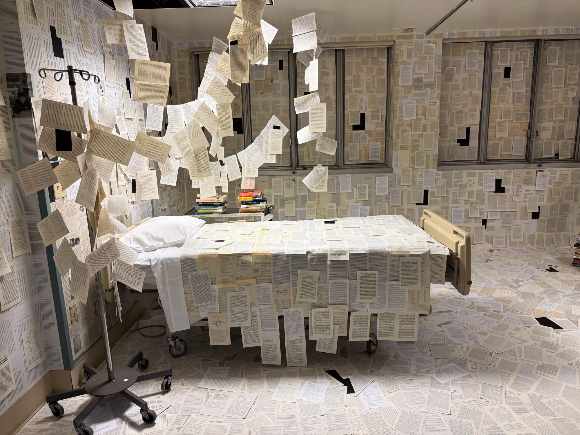 a hospital room installation transformed by pages of books on every surface