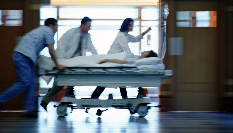 a motion-blurred image of medical workers pushing a patient on a gurney down a hospital corridor