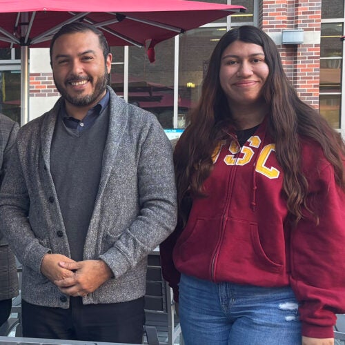 Bearded man in glasses and cardigan stands with woman in USC zippered hoodie