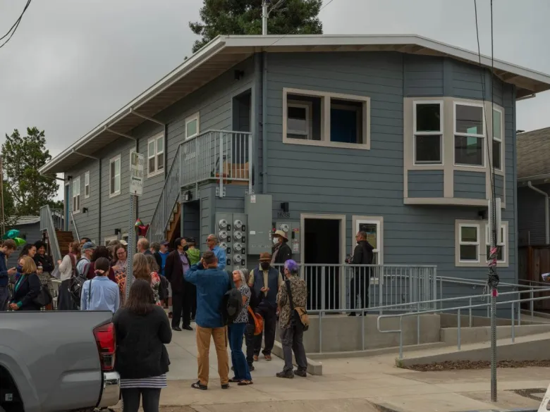 Several people mill around outside a blue, two-story, recently renovated apartment building in Berkeley.