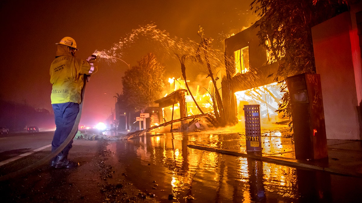A firefighter holding a hose spraying water at a fire near Pacific Coast Highway in Los Angeles