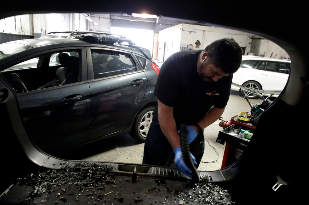Hector Hernandez vacuums up broken glass from a vehicle in preparation for replacing its rear window after a burglary.