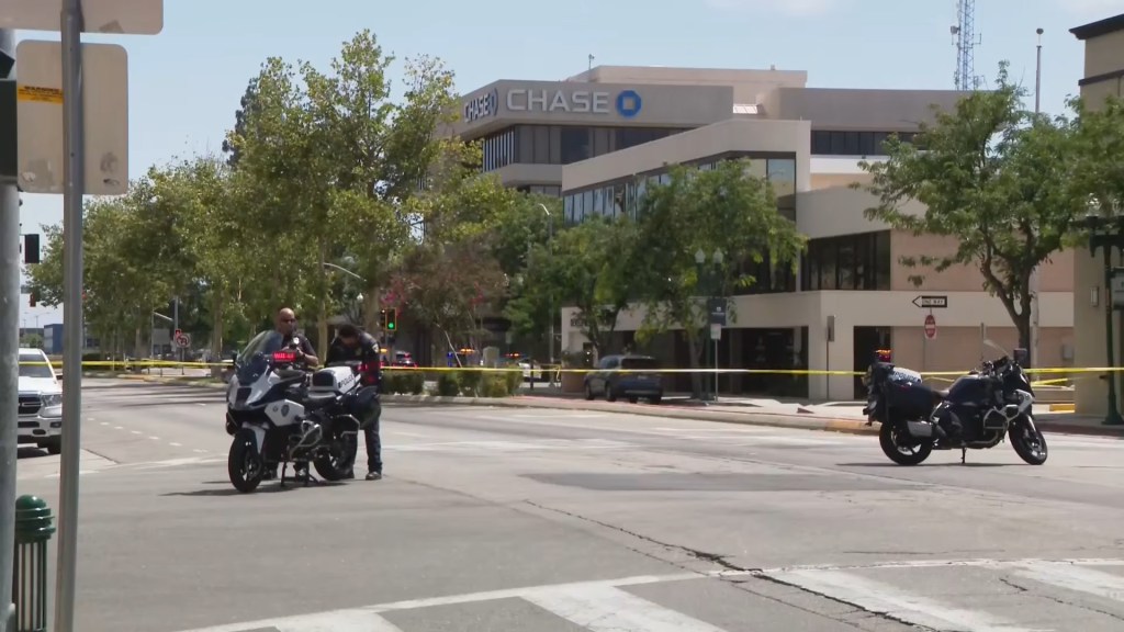 Police officers and motorcycles on a street blocked with yellow tape, with a Chase Bank building in the background.