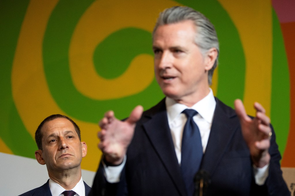 California Governor Gavin Newsom holding a press conference with San Francisco Mayor Daniel Lurie standing behind him.