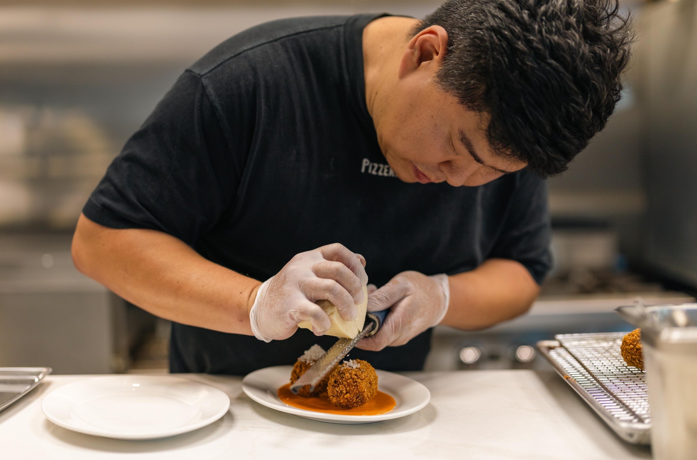 William Joo grating cheese over suppli at Pizzeria Sei.