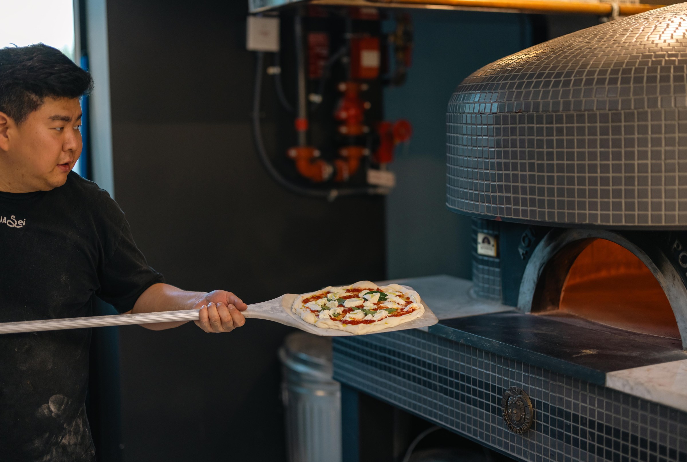 William Joo loading a pizza into the oven at Pizzeria Sei.