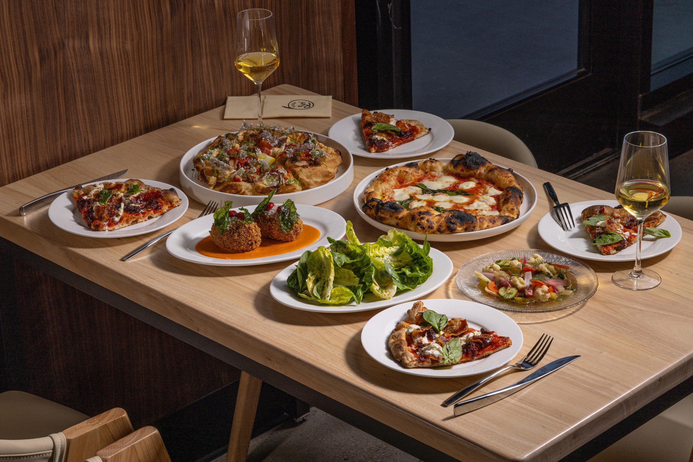 Spread of dishes including pizza and salad on a table at Pizzeria Sei.