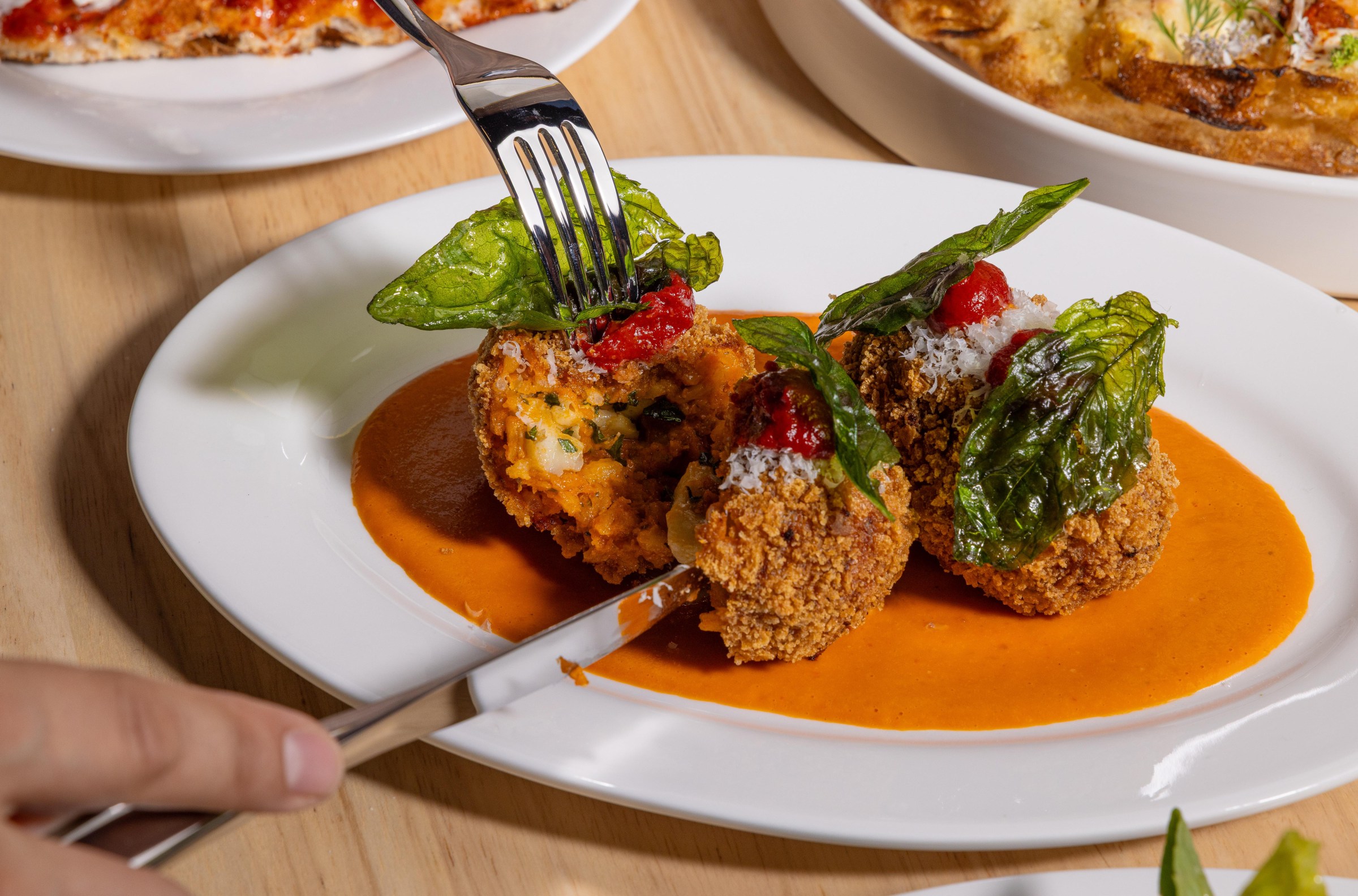 Knife and fork cutting into suppli at Pizzeria Sei.