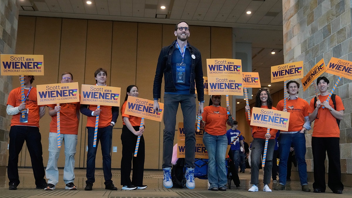 Scott Wiener jumping in the air while posing for photos with a group of people.