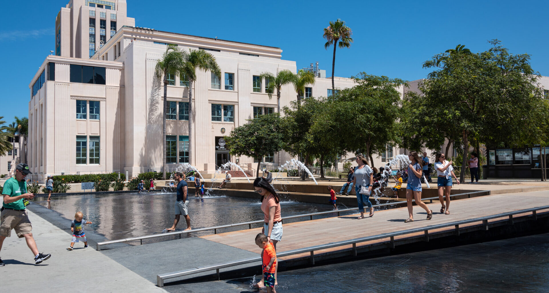 Photo of unidentified mother and son enjoying a warm summer day in the fountain at Waterfront Park in front of a County Administrative Building.