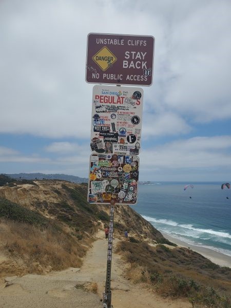A sign posted near the entrance of the Citizens Trail above Black's Beach is often covered in stickers. (Ashley Mackin-Solomon)