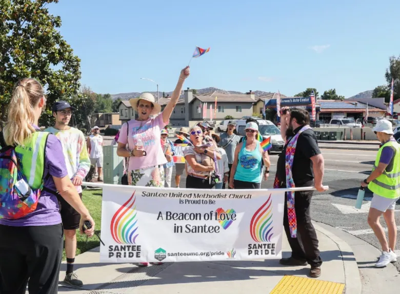 A banner reads "A beacon of love in Santee." Two people hold it while marchers in a residential area hold flags and even a dog.