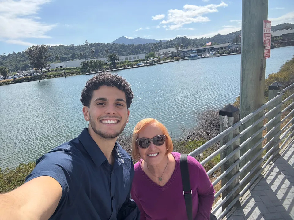 A young man and an older woman taking a selfie near a stretch of water.