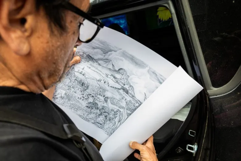 A person holding and examining a detailed black and white sketch or map while standing next to an open car door.