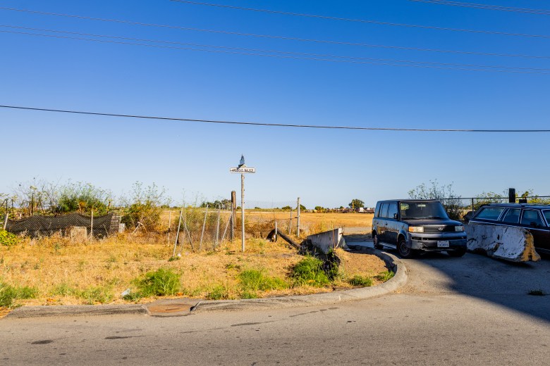 A vacant, grassy lot with a wooden post, an old van, and a station wagon parked nearby under a clear blue sky.