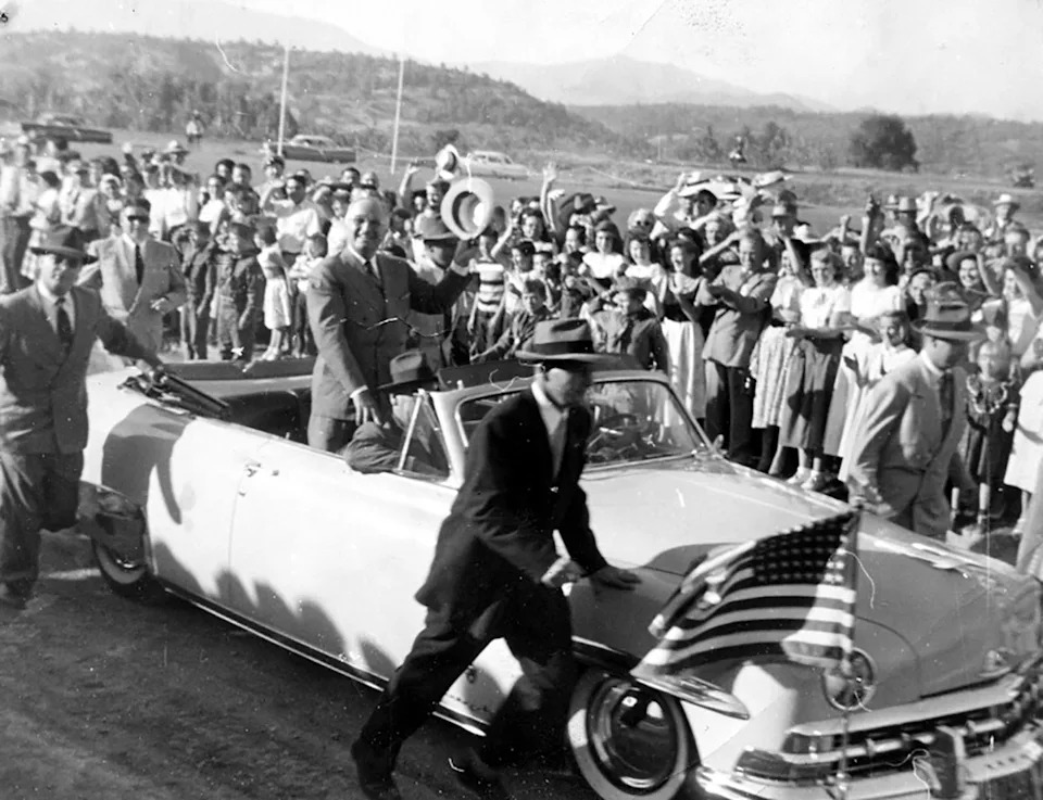 From the back seat of a convertible, President Harry S. Truman, hat in hand, waves to the crowd gathered to greet him on the football field at Shasta College, Redding, California. President Truman was on a Western trip at that time campaigning for Adlai Stevenson. Donor: Stella Dillenbeck.