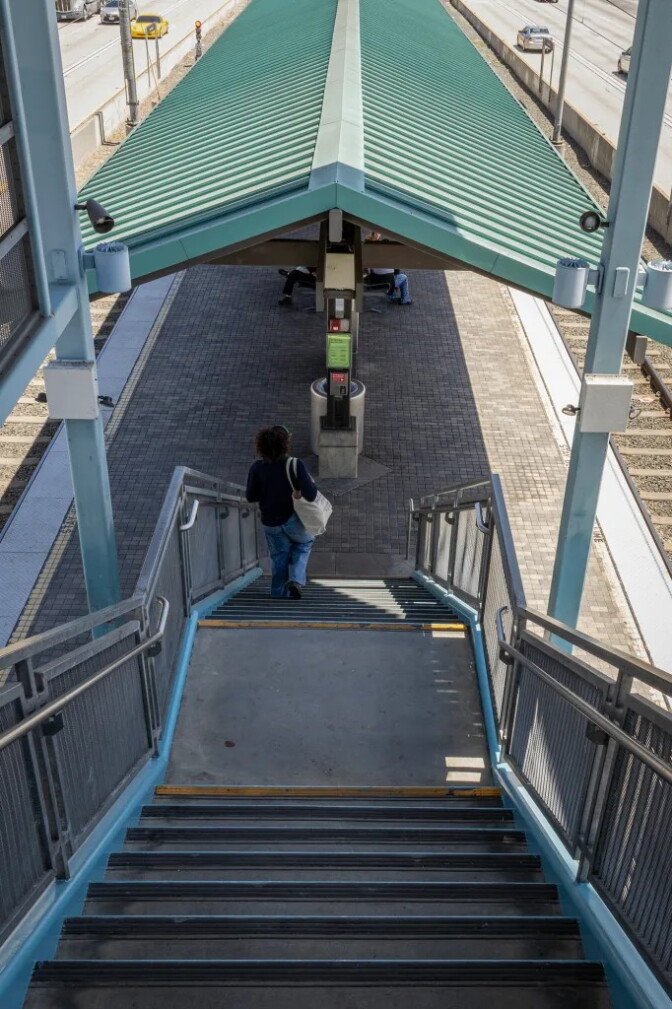 A woman is pictured from behind at the bottom of a set of stairs, outdoors. To her left and right are train tracks.