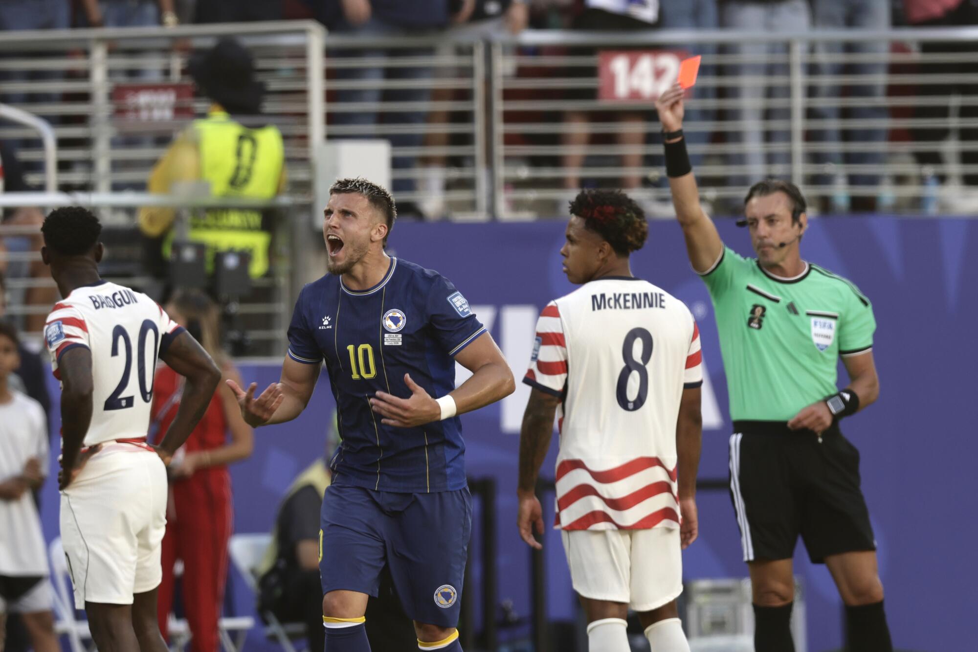 A referee gives a red card to U.S. forward Folarin Balogun while Bosnia-Herzegovina's Ermedin Demirovic reacts.