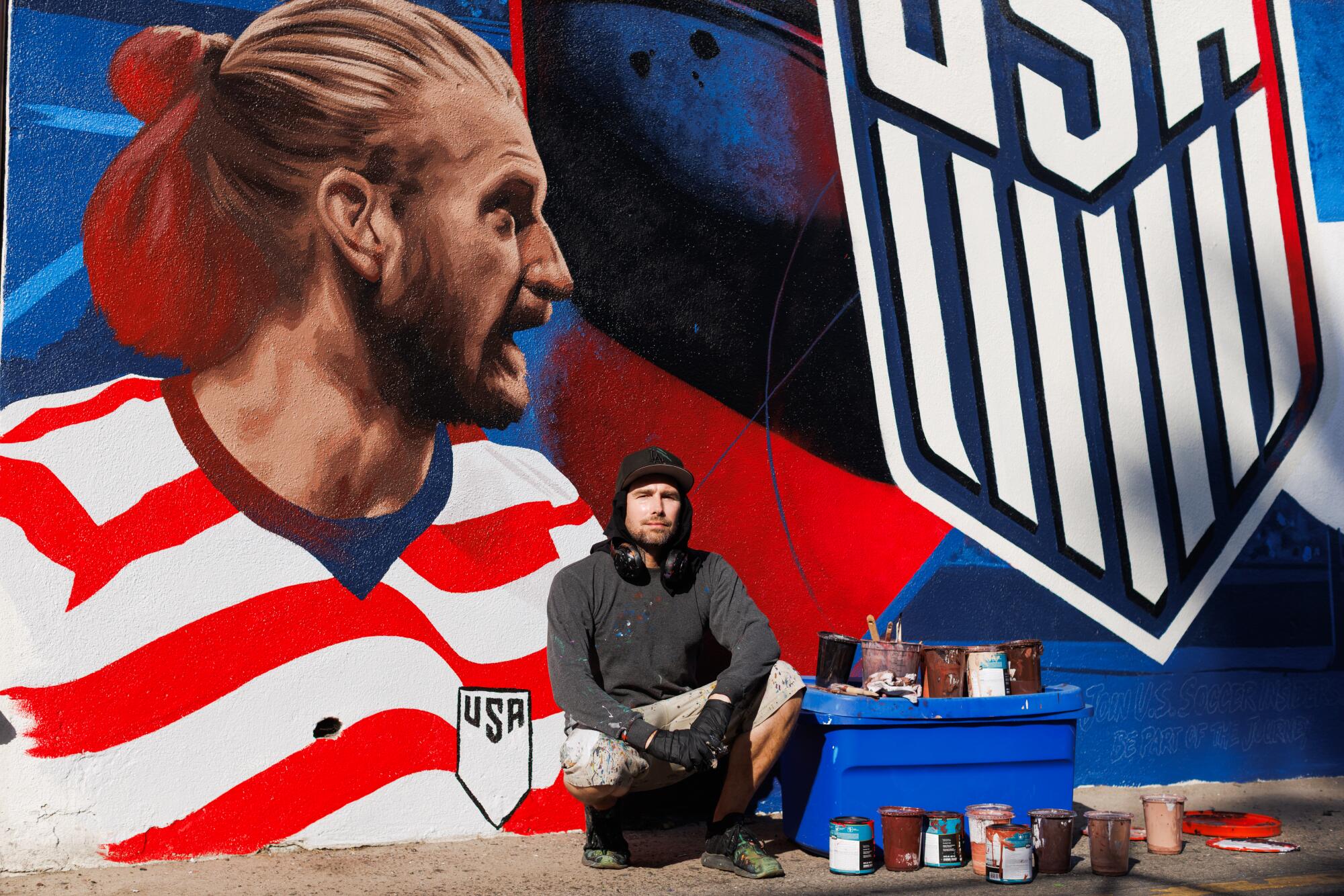 A person sits in front of a World Cup mural he painted.