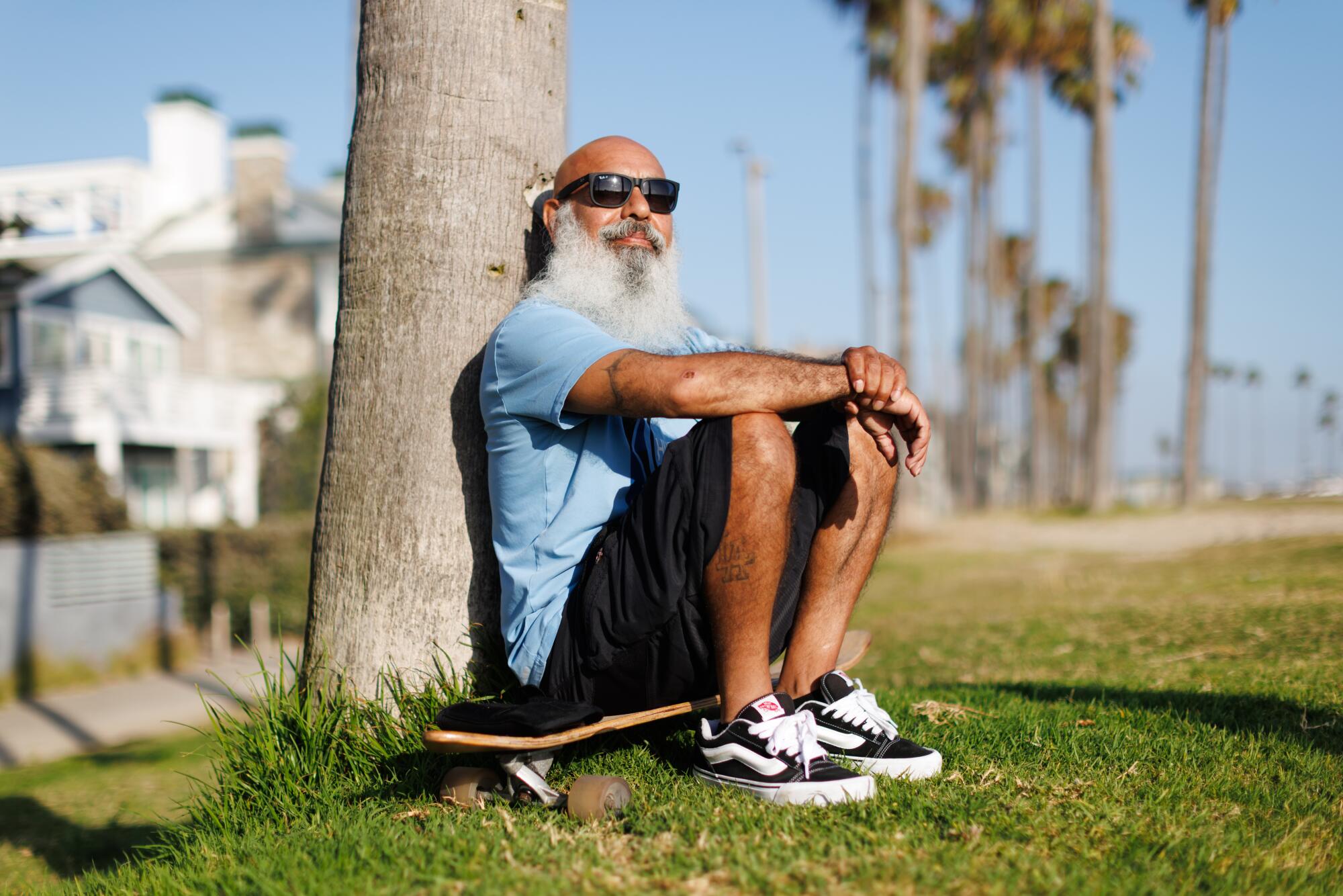 A person sits on their skateboard against a palm tree at Venice Beach.