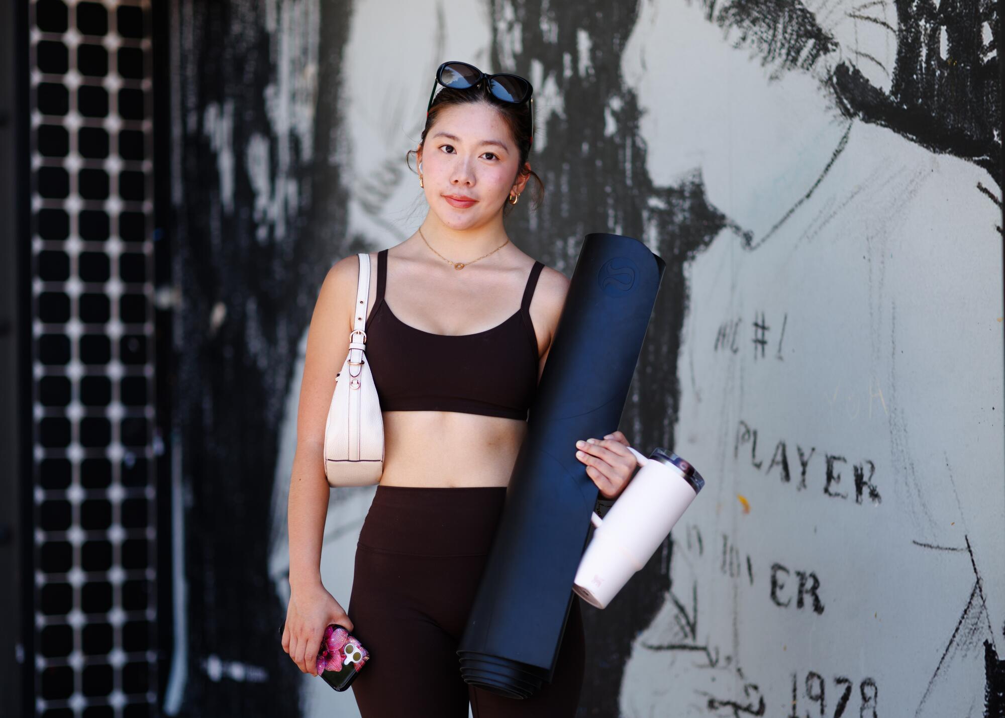 A person stands by a mural in Westood holding a yoga mat.