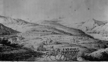 A group of soldiers march in formation near a large building by mountains, with officers on horseback and a ship anchored by the shore.