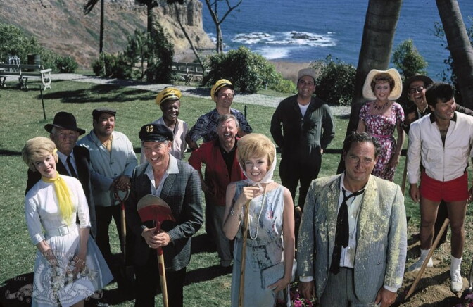 A group of people in a grassy park overlooking the ocean face the camera and smile. 