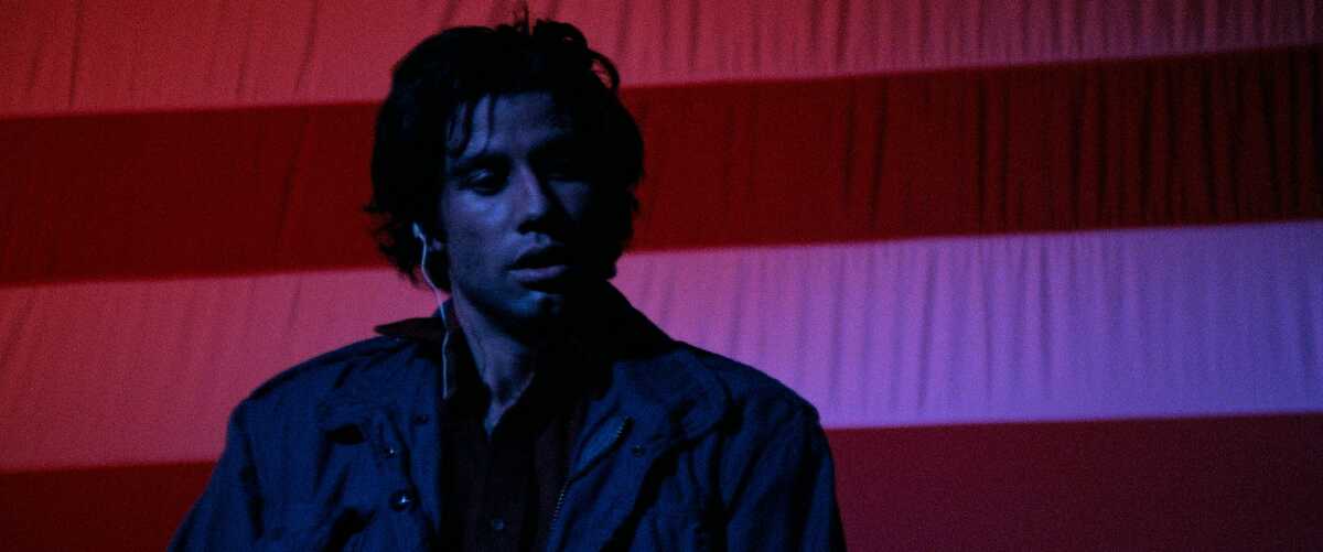 A man with an ear monitor stands in front of an American flag.
