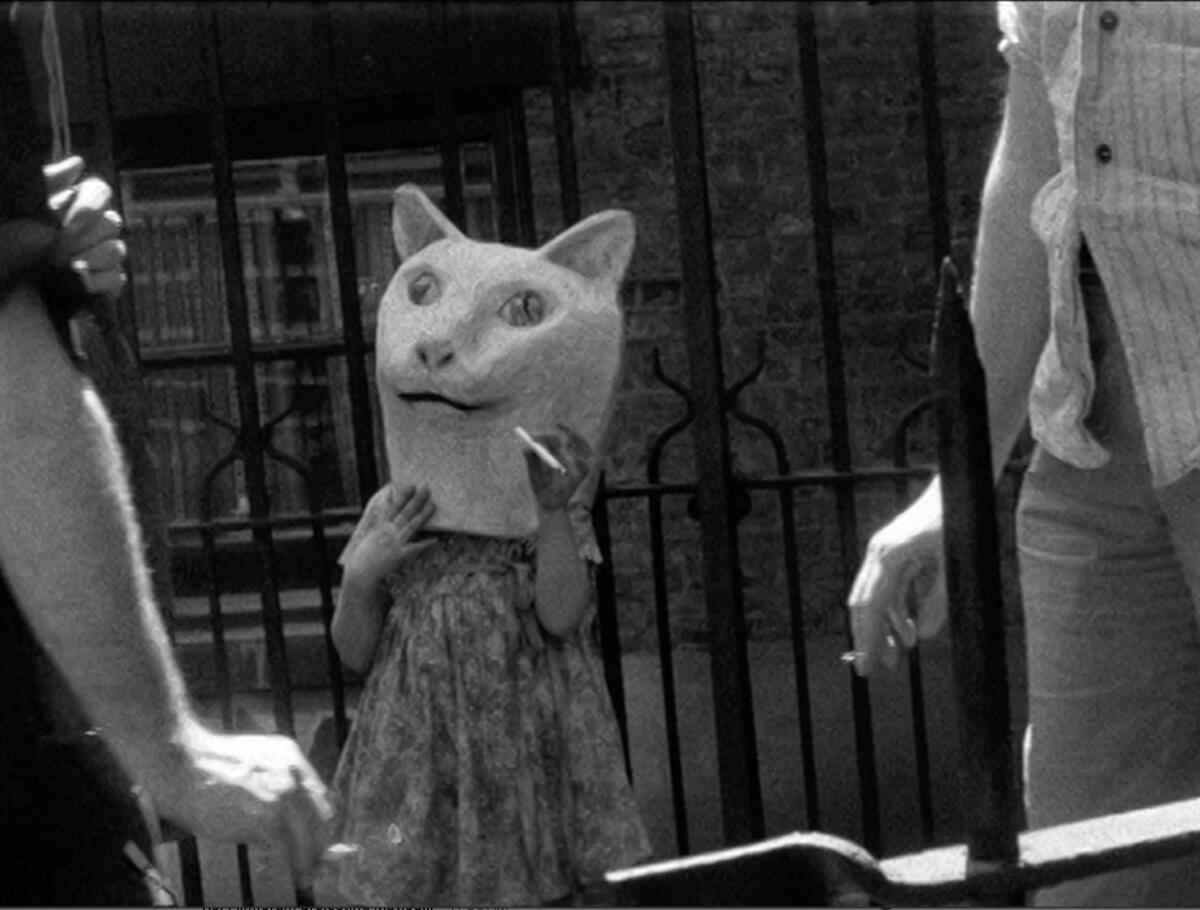 A strange cat costume is worn by a woman in front of an iron gate.