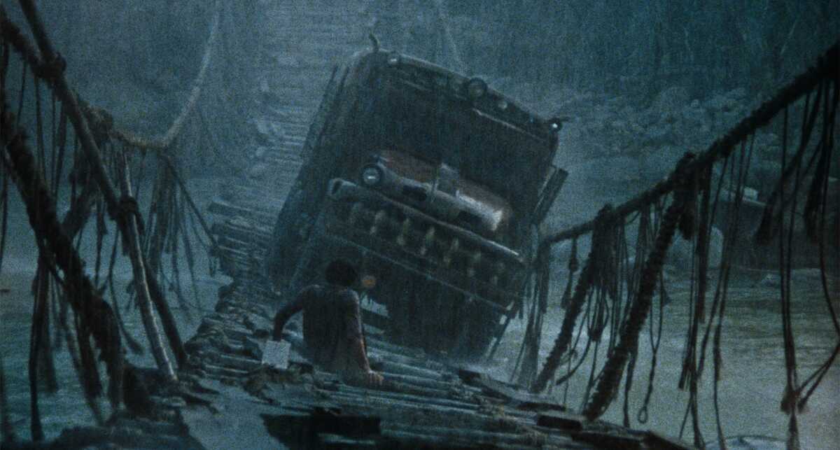A truck teeters on a rope bridge in a rainstorm in the jungle.