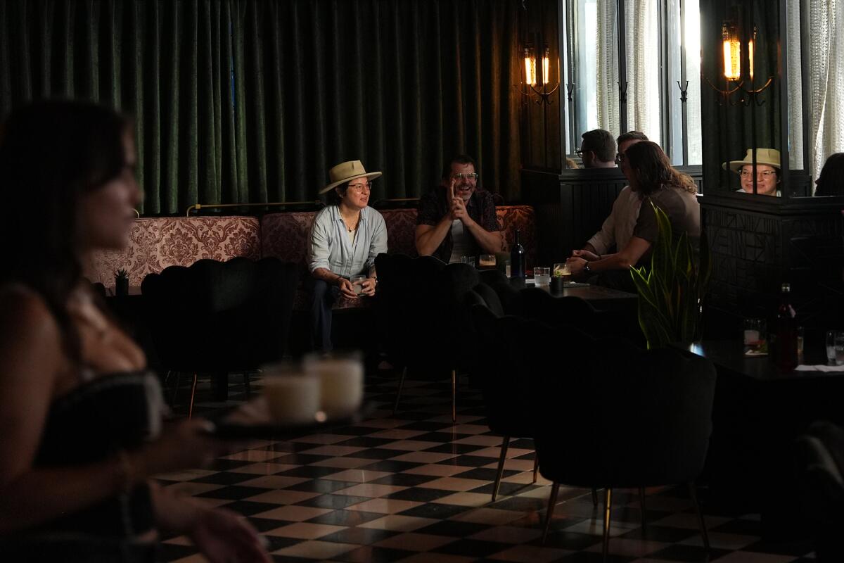A woman with hat joins friends at bar. 