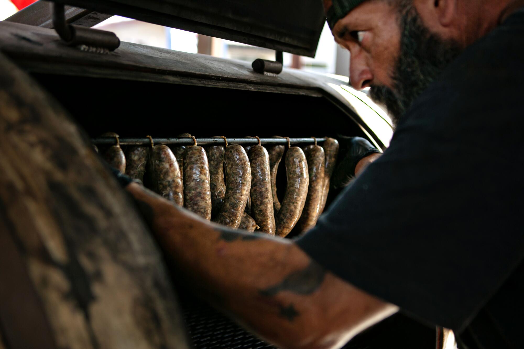 One of the pitmasters at Heritage Barbecue loads a smoker with sausages.