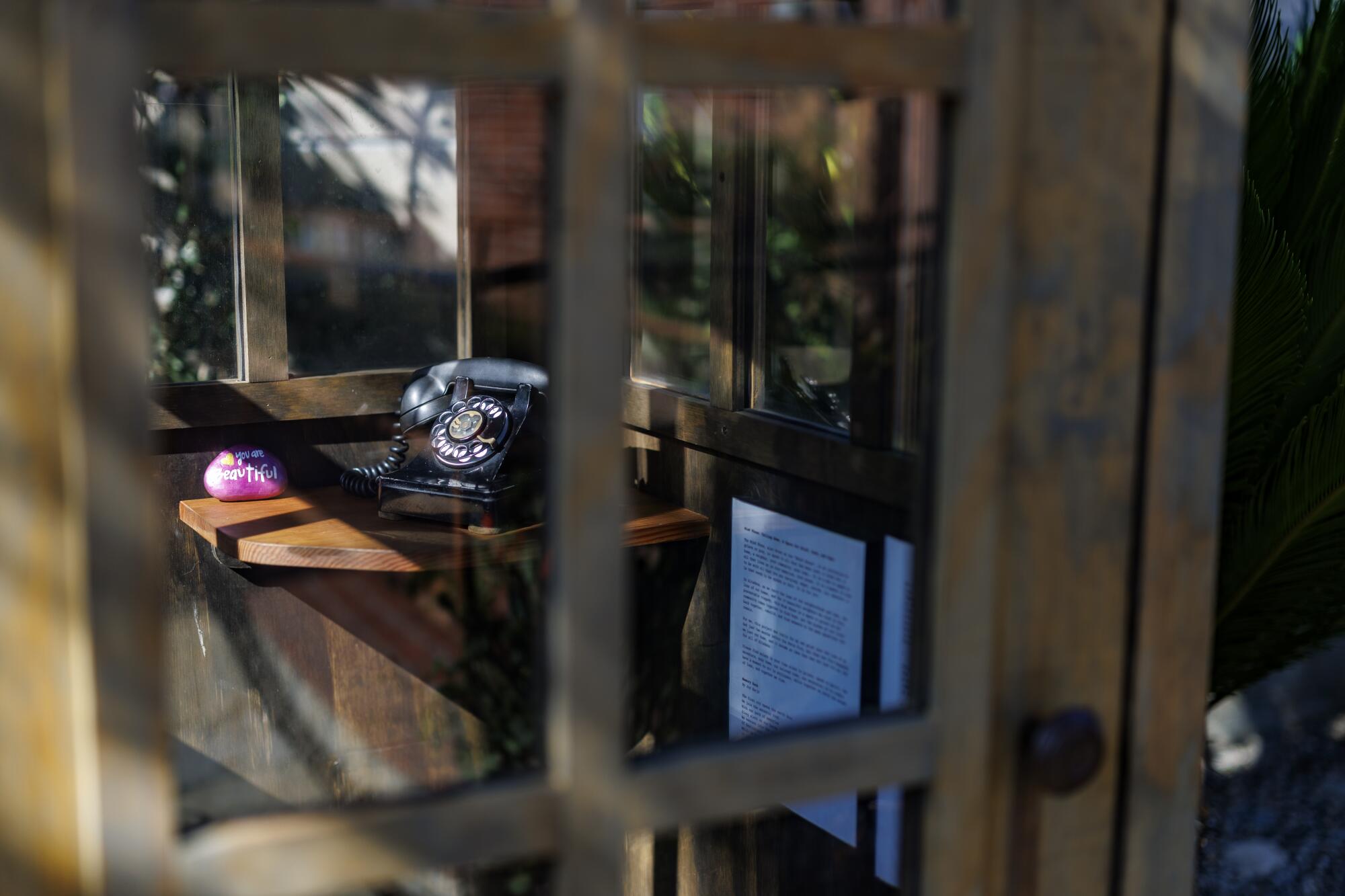 An old black rotary phone sits inside a wind phone booth.
