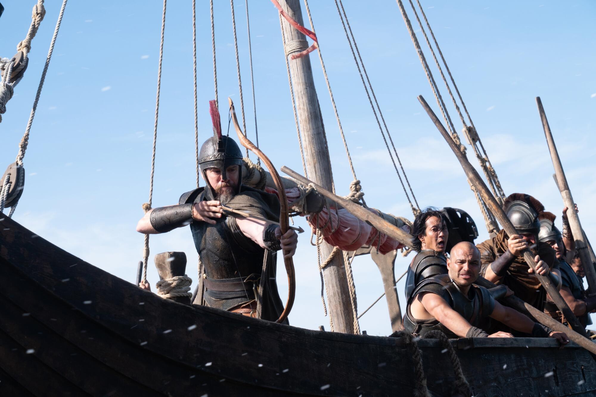 A soldier in a helmet aims a bow and arrow on the deck of a boat.