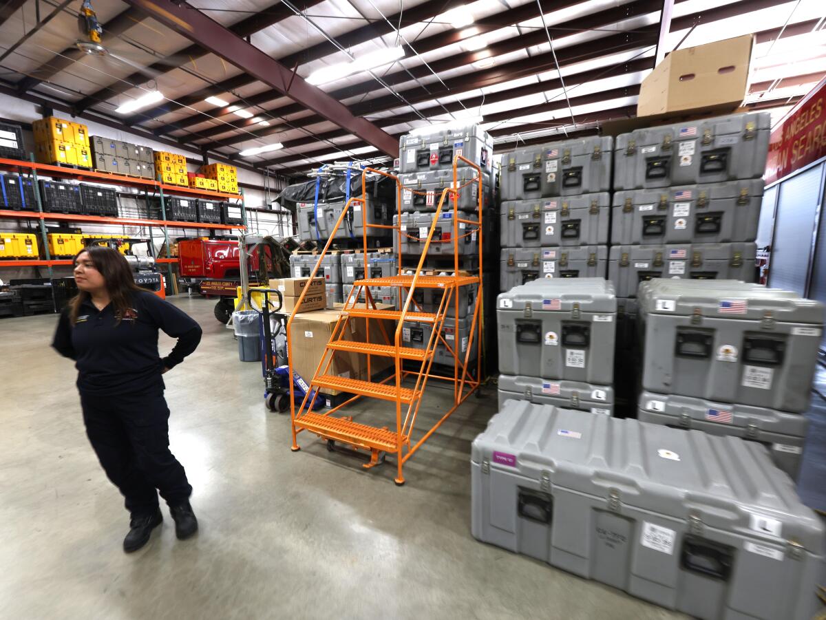 A woman stands next to stacks of crates in a warehouse.