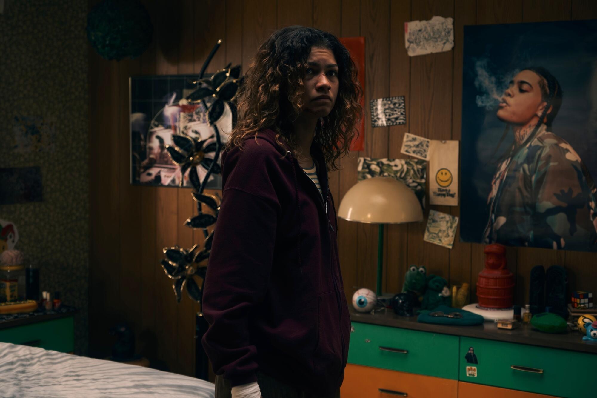 Zendaya wearing a dark zip-up hoodie in a bedroom 