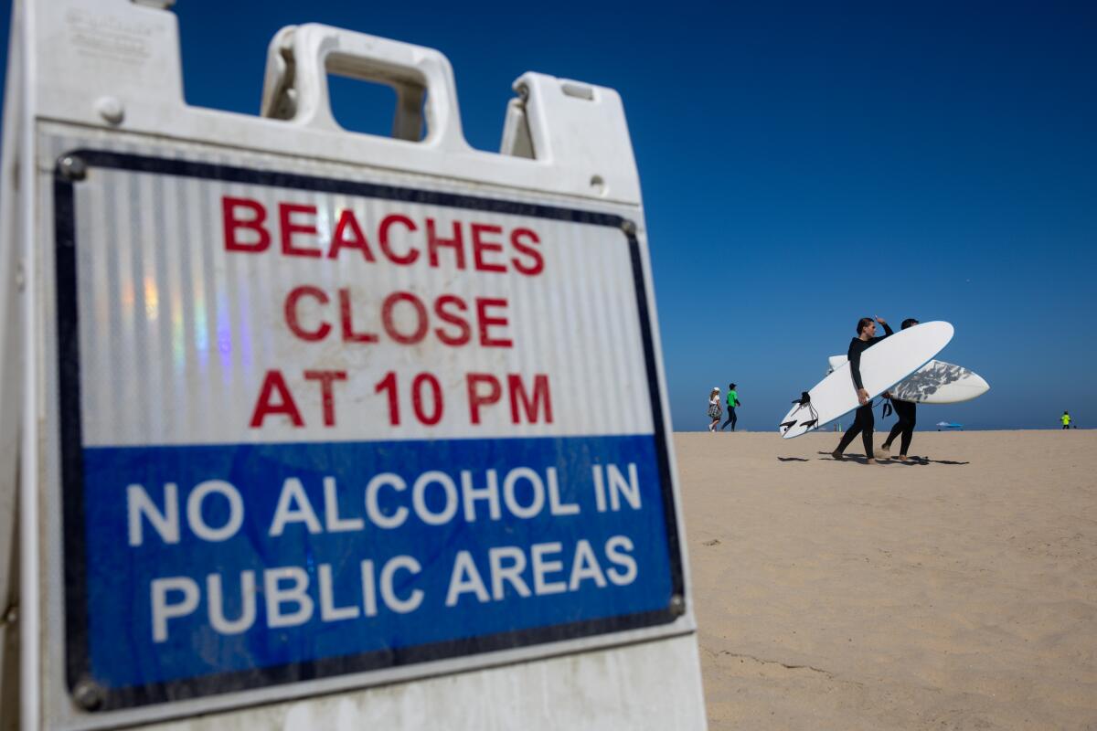 Surfers walk past a sign along W. Ocean Front on July 6 in Newport Beach.