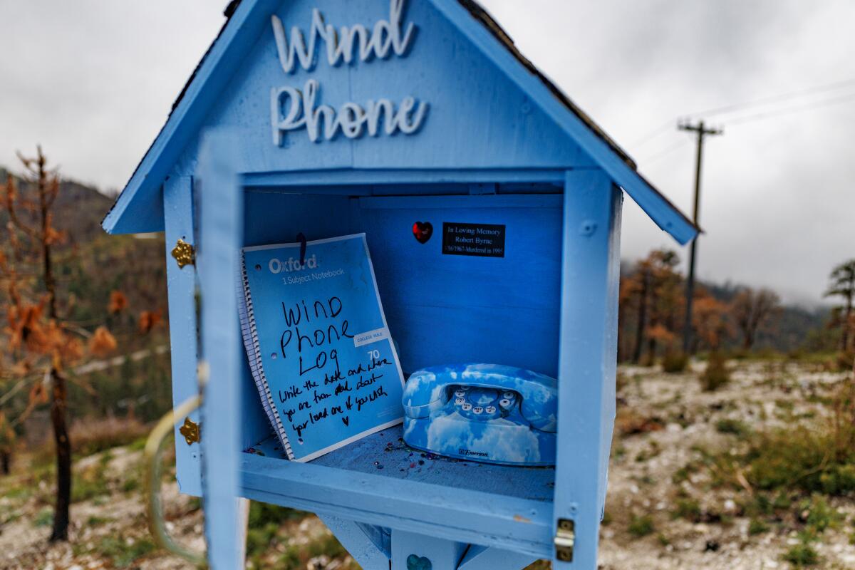 A notebook stands inside the wind phone structure in the mountainous terrain on a hillside near a road side turnout 