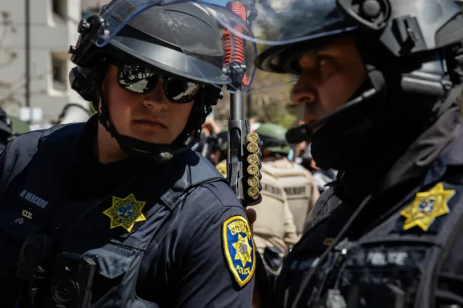 A close up of two police officers talking with one another with more in the background.