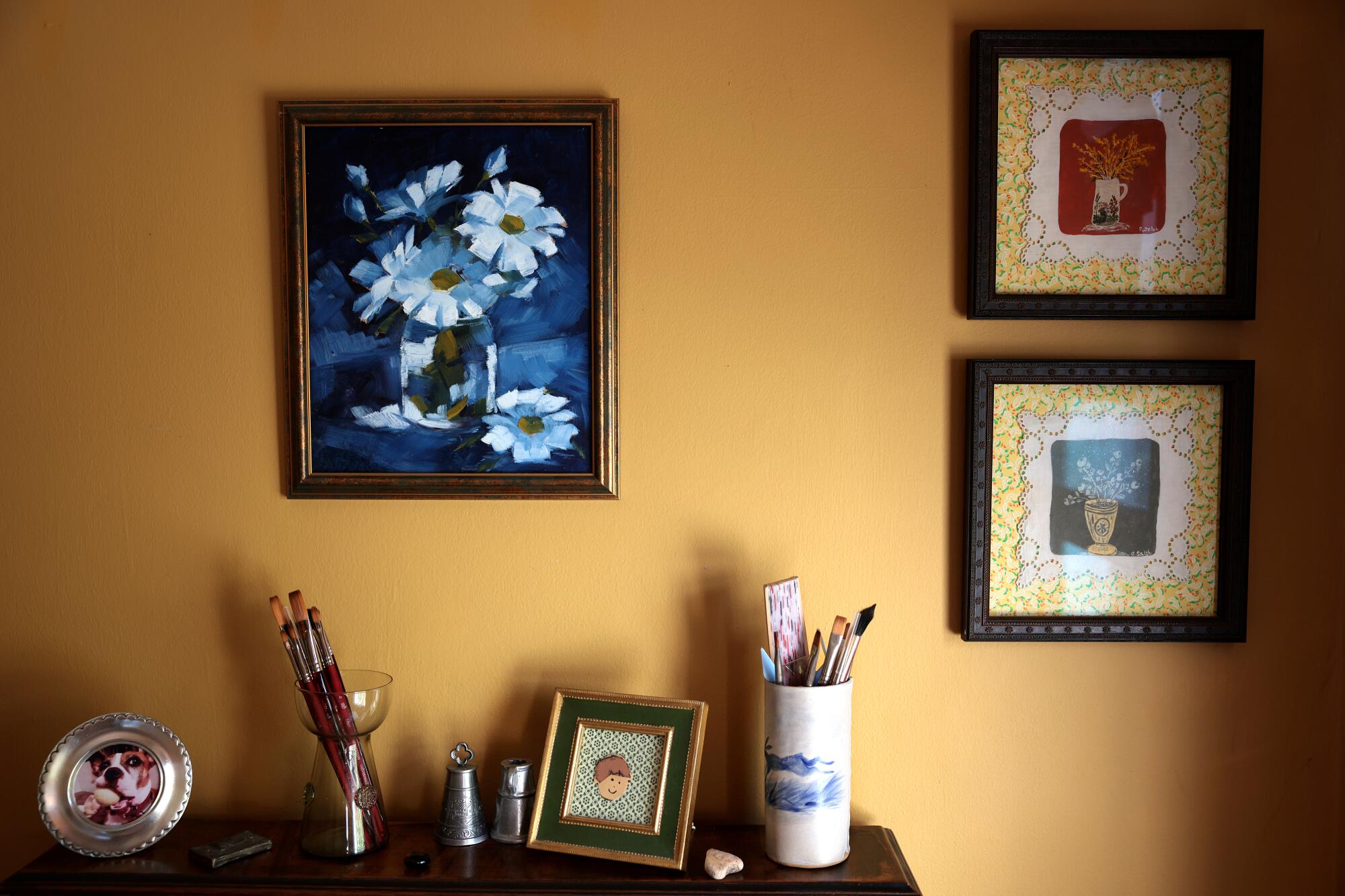 Paintings on a wall above a dresser with artwork.