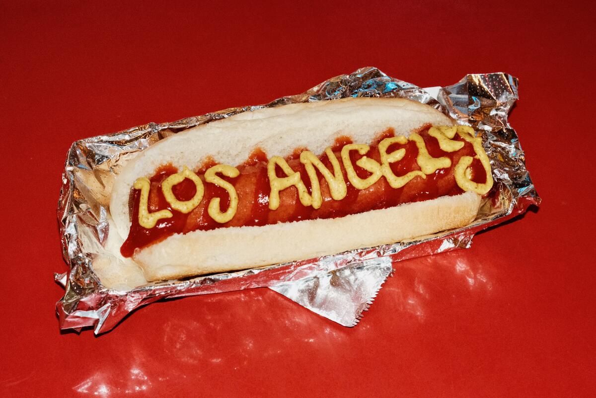 A hot dog with "Los Angeles" written in ketchup and mustard at Walt's Bar on a red bar top.