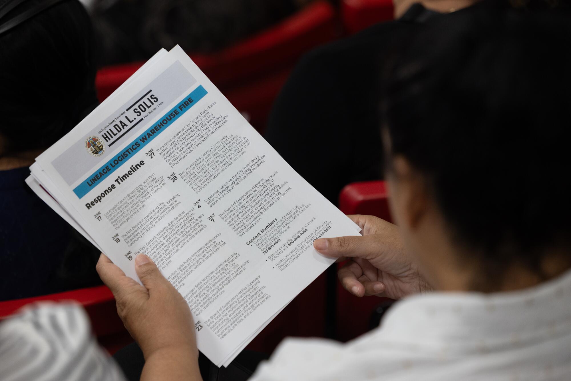 During a town hall, an audience member holds a pamphlet about the response to the warehouse fire.