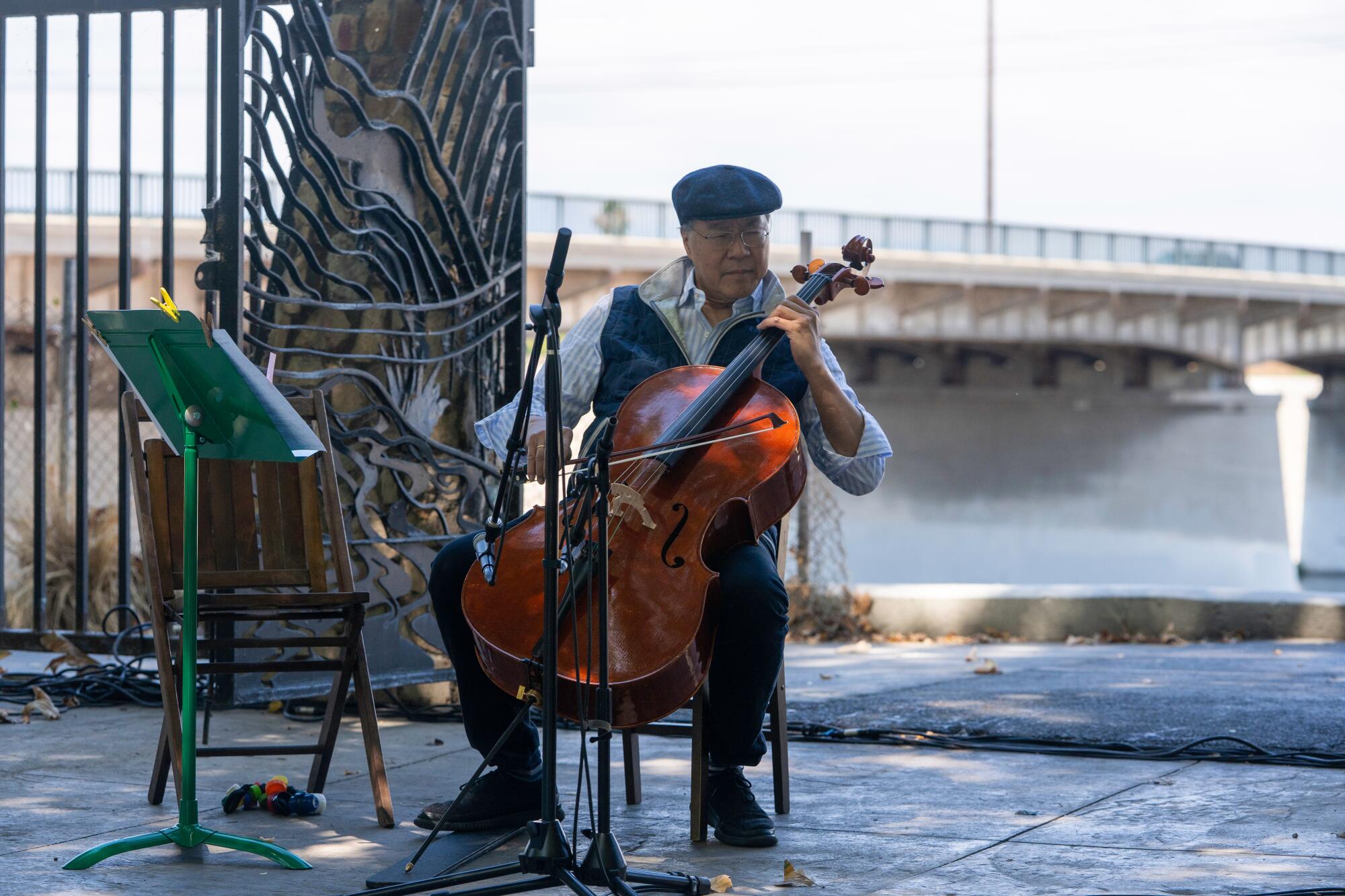 Yo-Yo Ma, in a cap and vest, plays cello in front of the L.A. River basin.