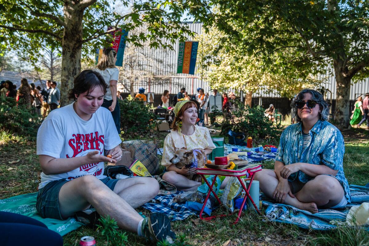 Three women picnic on a blanket in a park.