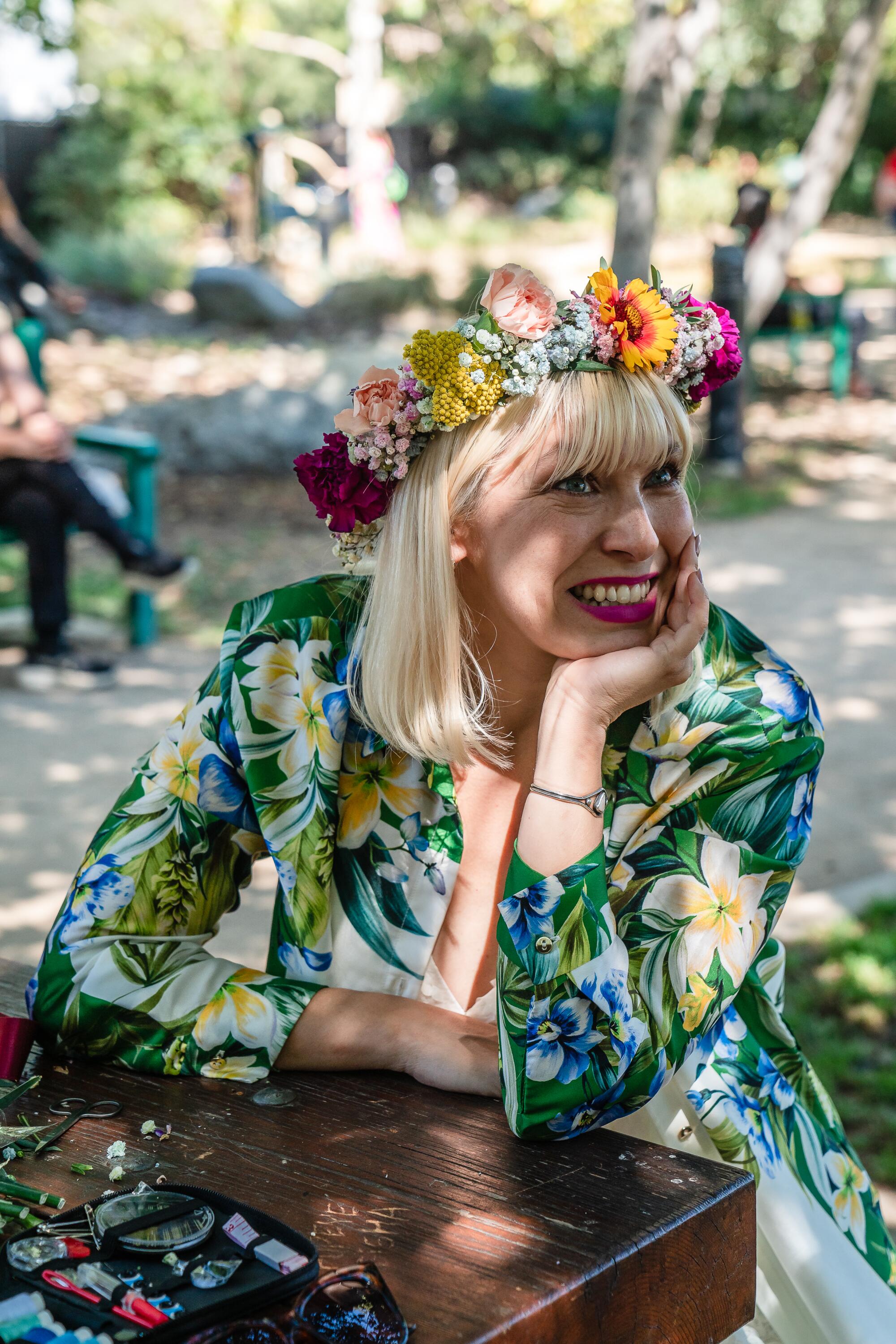 A woman in a flowery green dress wears a flower crown.
