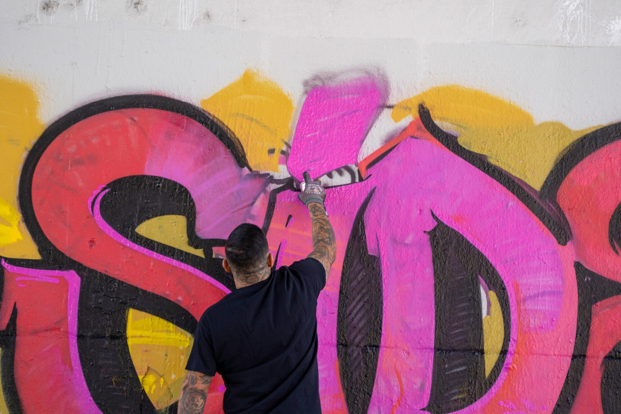 A man spray paints blow letters on a wall.