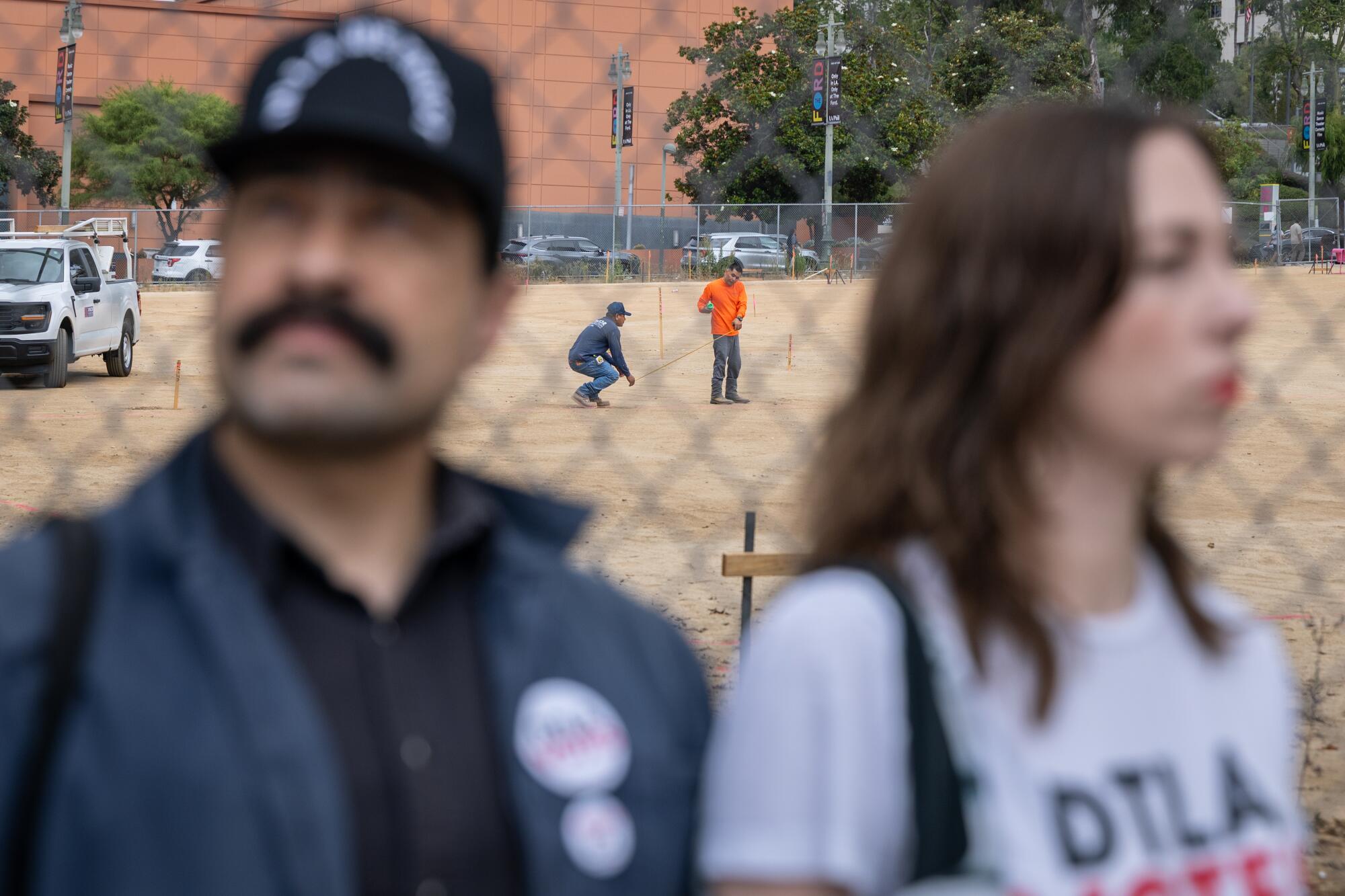Workers behind two people and a chain-linked fence.