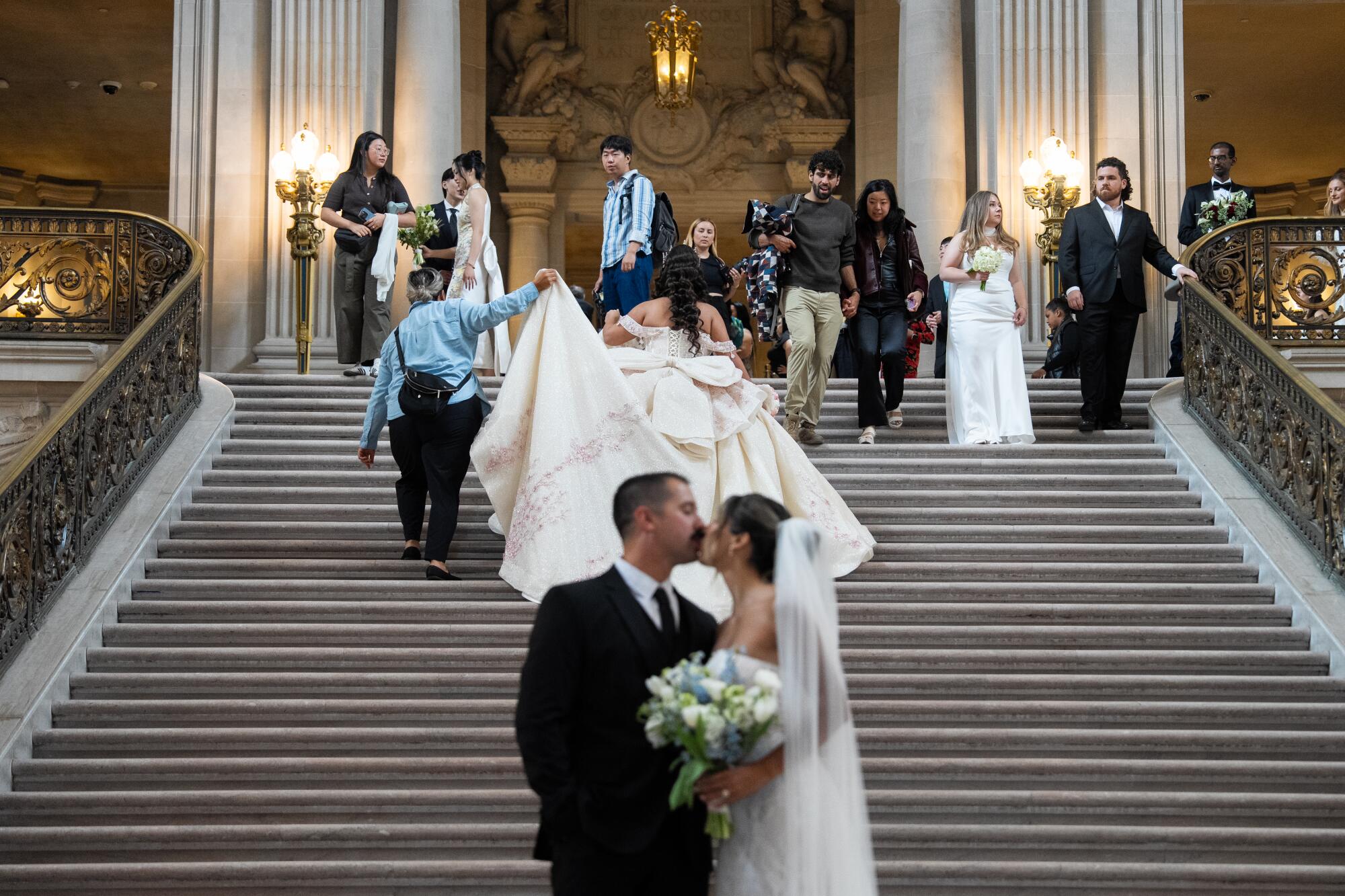 Several brides and grooms stand around a grand staircase.